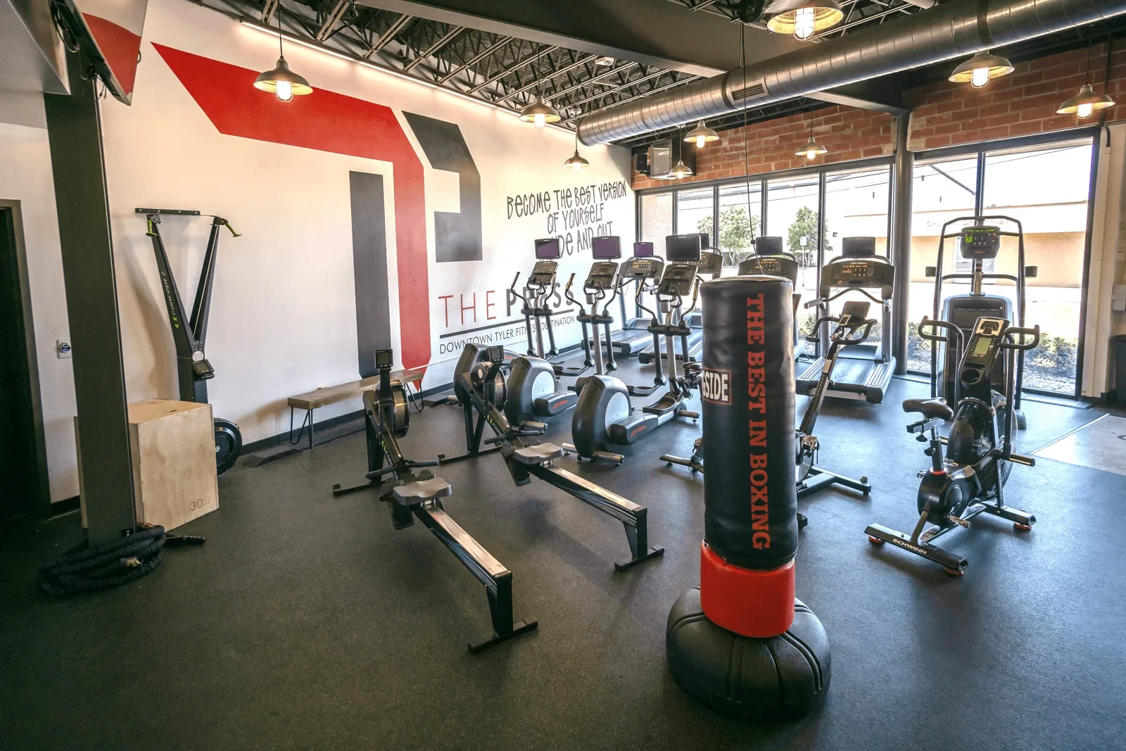 Inside The Press: rowers and cardio machines on black rubber flooring in front of an exposed-brick wall