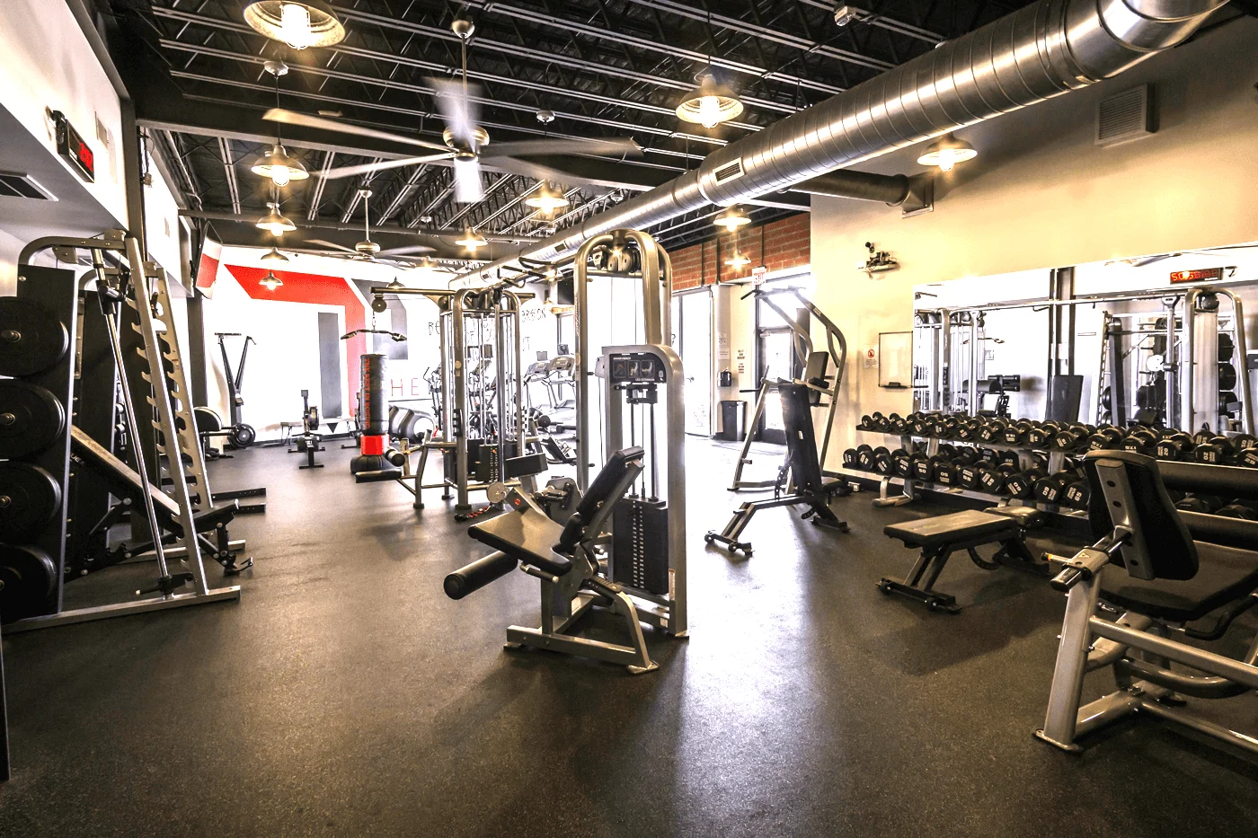 Free weights area with dumbbells, benches and industrial factory lighting